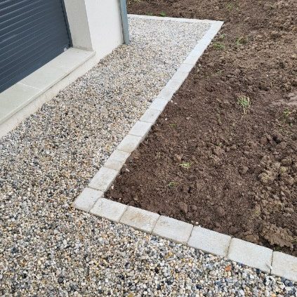 Allée en gravier bordée de pavés, transition vers un sol nu.